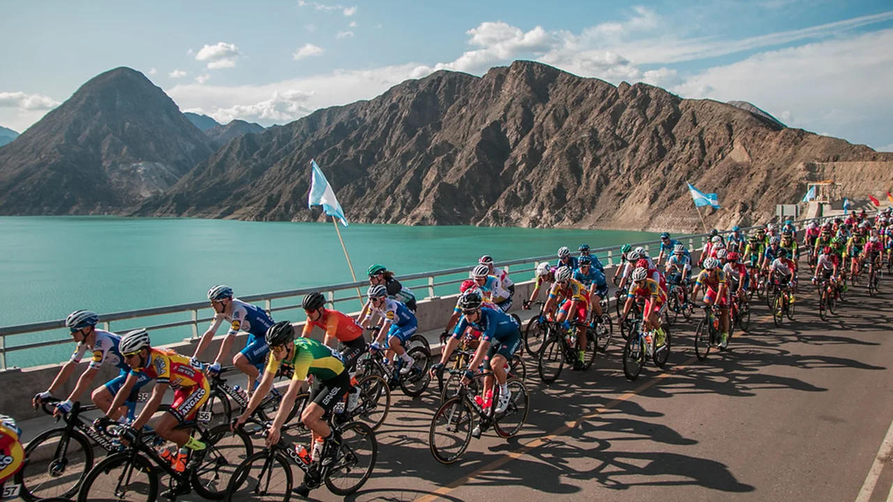 Road cyclists beside a reservoir and the mountains of San Juan